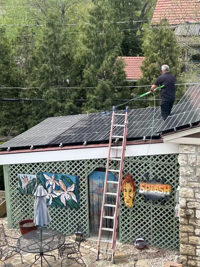 Solar panel cleaning by Sparkle Window Cleaners — Worker on ladder cleaning roof-mounted solar panels.