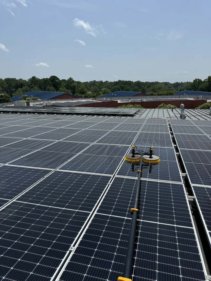 Solar panel cleaning by Sparkle Window Cleaners — Dusty rooftop solar array with cleaning brush